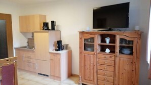 A compact living space with a kitchenette, a flat-screen TV, and a wooden cabinet with drawers. - Ferienwohnung am Schöneberg Nähe Nürburgring (Heckenbach)