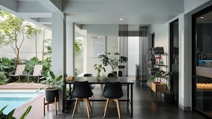 A modern dining area with a pool view, a sign indicating the location of the toilet, and a variety of plants. - POR Arak (Chiang Mai)