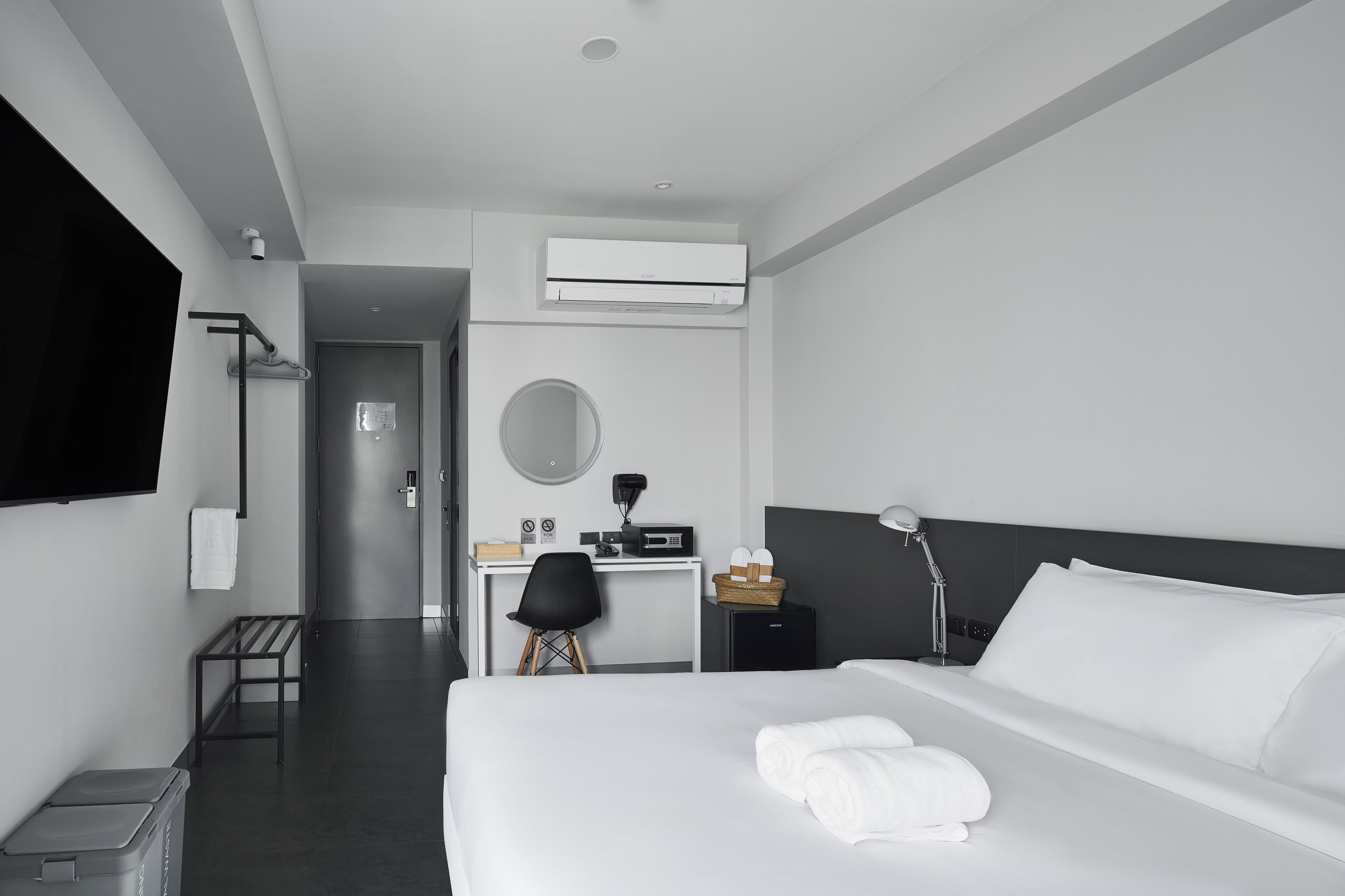 Una habitación de hotel moderna con cama, escritorio, silla, televisor y aire acondicionado.