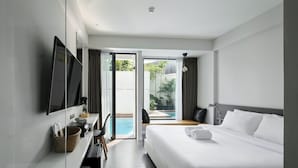 A modern hotel room with a large bed, a desk with a computer, and a view of a swimming pool and garden. - POR Arak (Chiang Mai)