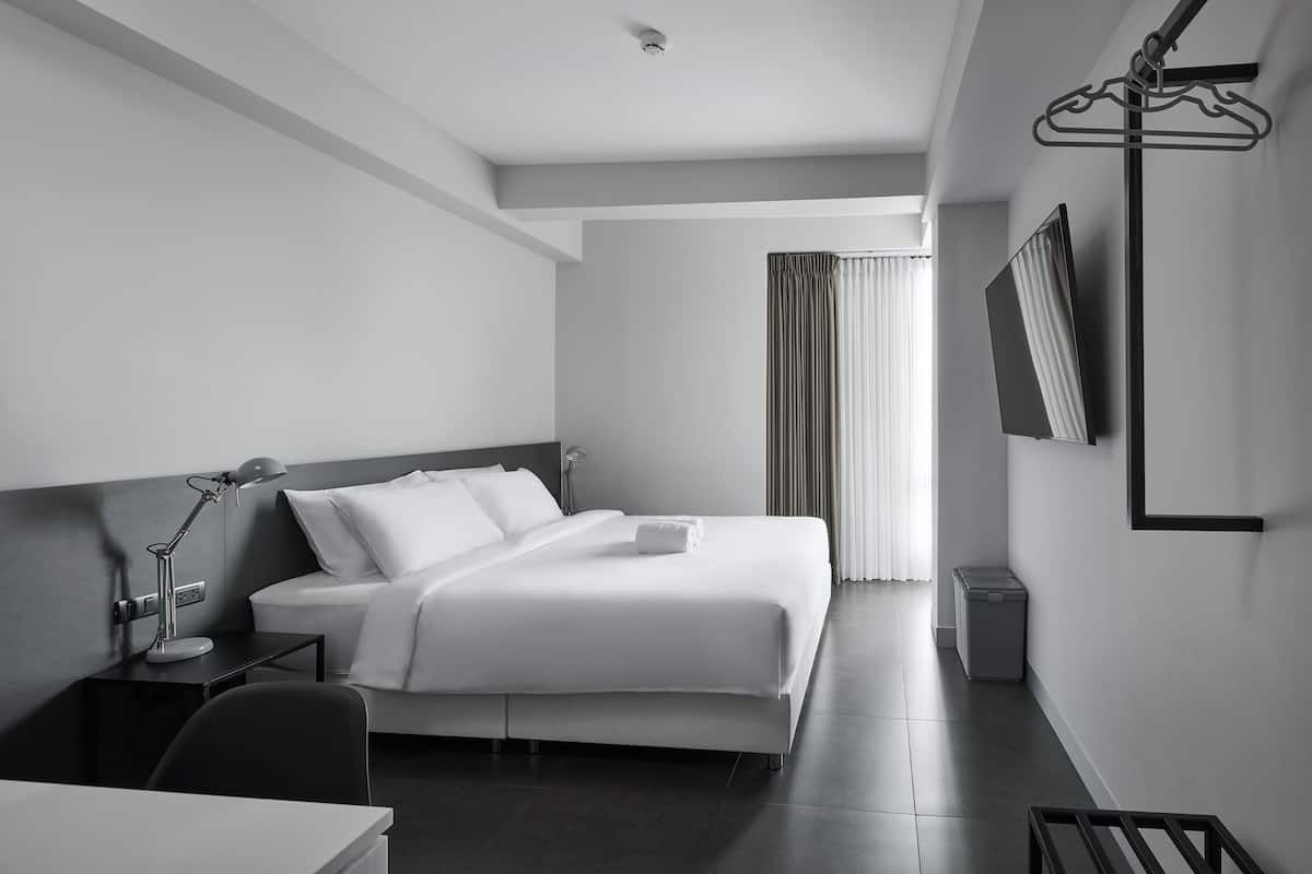 A modern hotel room with a neatly made bed, a desk with a lamp, a TV mounted on the wall, and a walk-in closet.