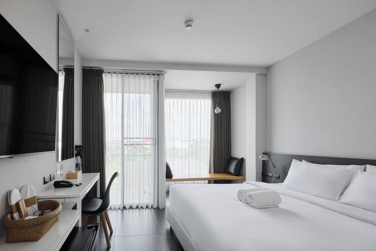 A modern hotel room with a large bed, a desk with a chair, a small table, and a TV.