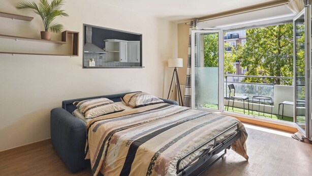 Un dormitorio con cama, una planta en maceta, un espejo y vistas a un balcón con mobiliario exterior.