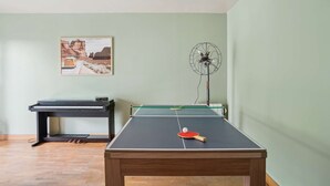 Una habitación con mesa de ping pong, piano y ventilador.