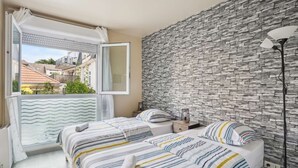 Un dormitorio con dos camas, una ventana con cortinas, una pared de piedra y una mesita de noche con lámpara.