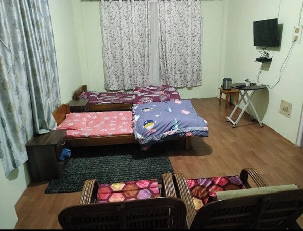 A bedroom with two single beds, a small table with a chair, a TV mounted on the wall, and a window with curtains. - Mondruk Homestay (Tawang)