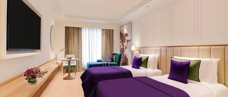 Habitación de hotel con dos camas, televisión, escritorio y ventana con cortinas.