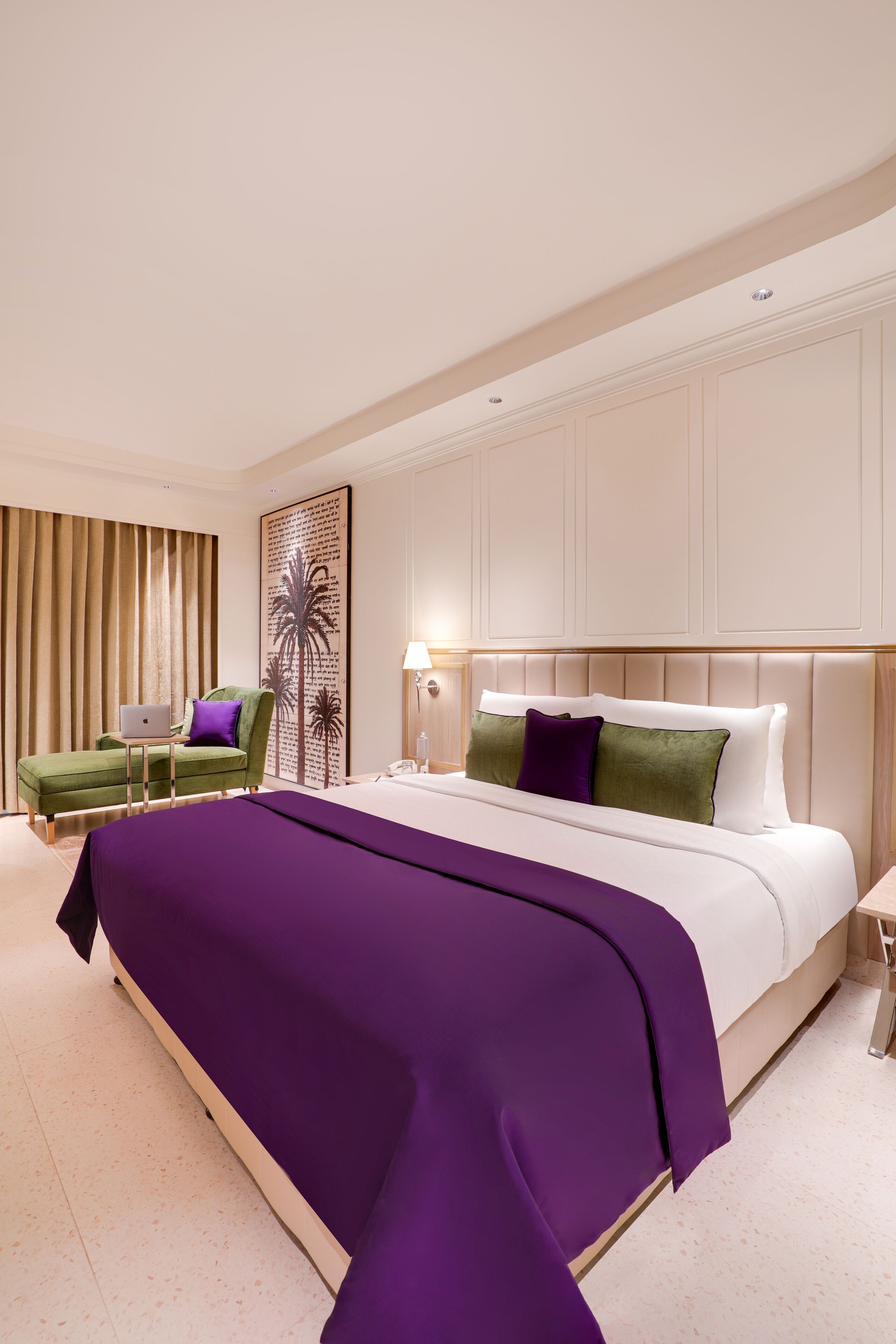 A hotel room with a large bed, a green armchair, a laptop, and a decorative wall panel.