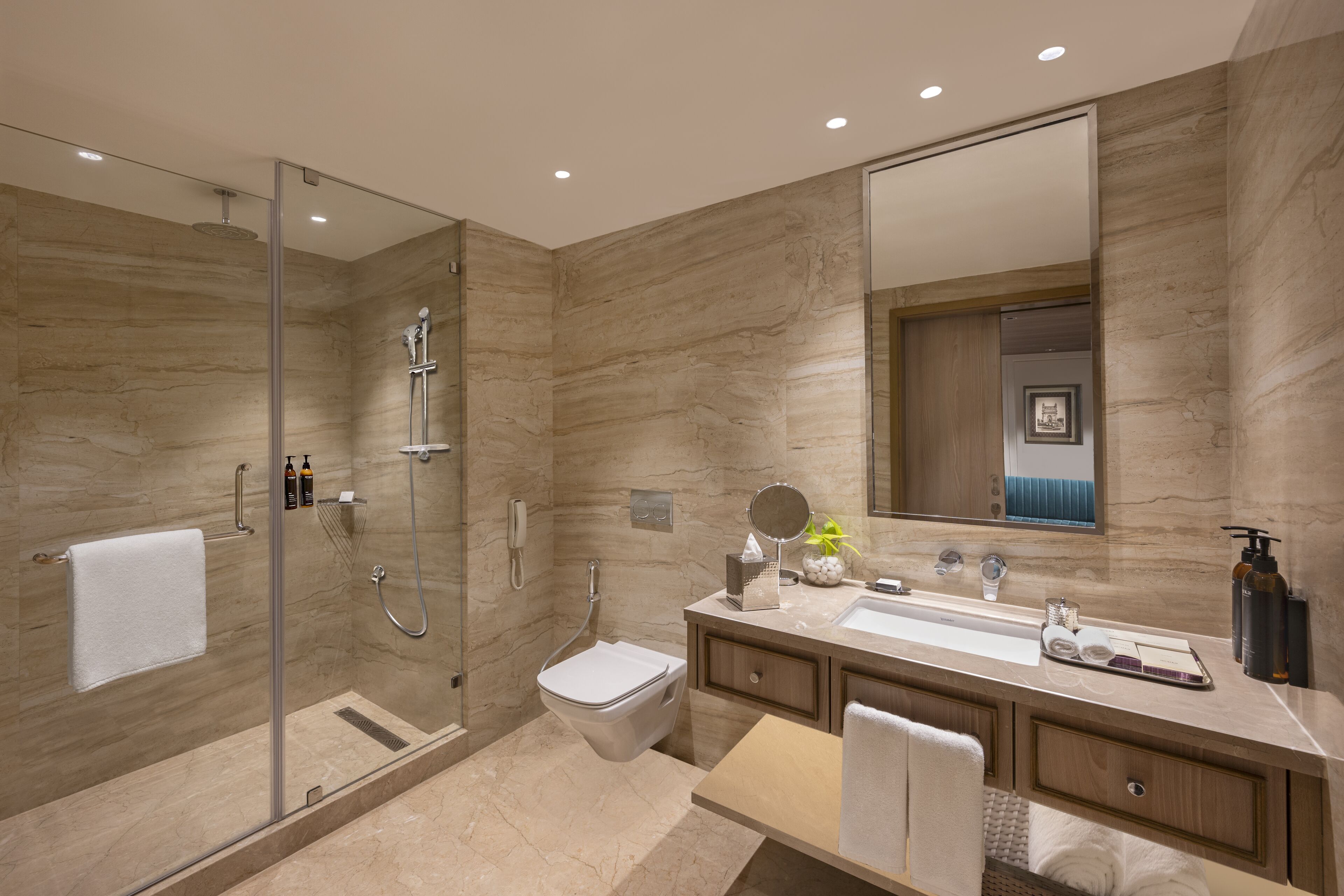 Un baño moderno con ducha envuelta en vidrio, inodoro, lavabo con tocador y un espejo grande.