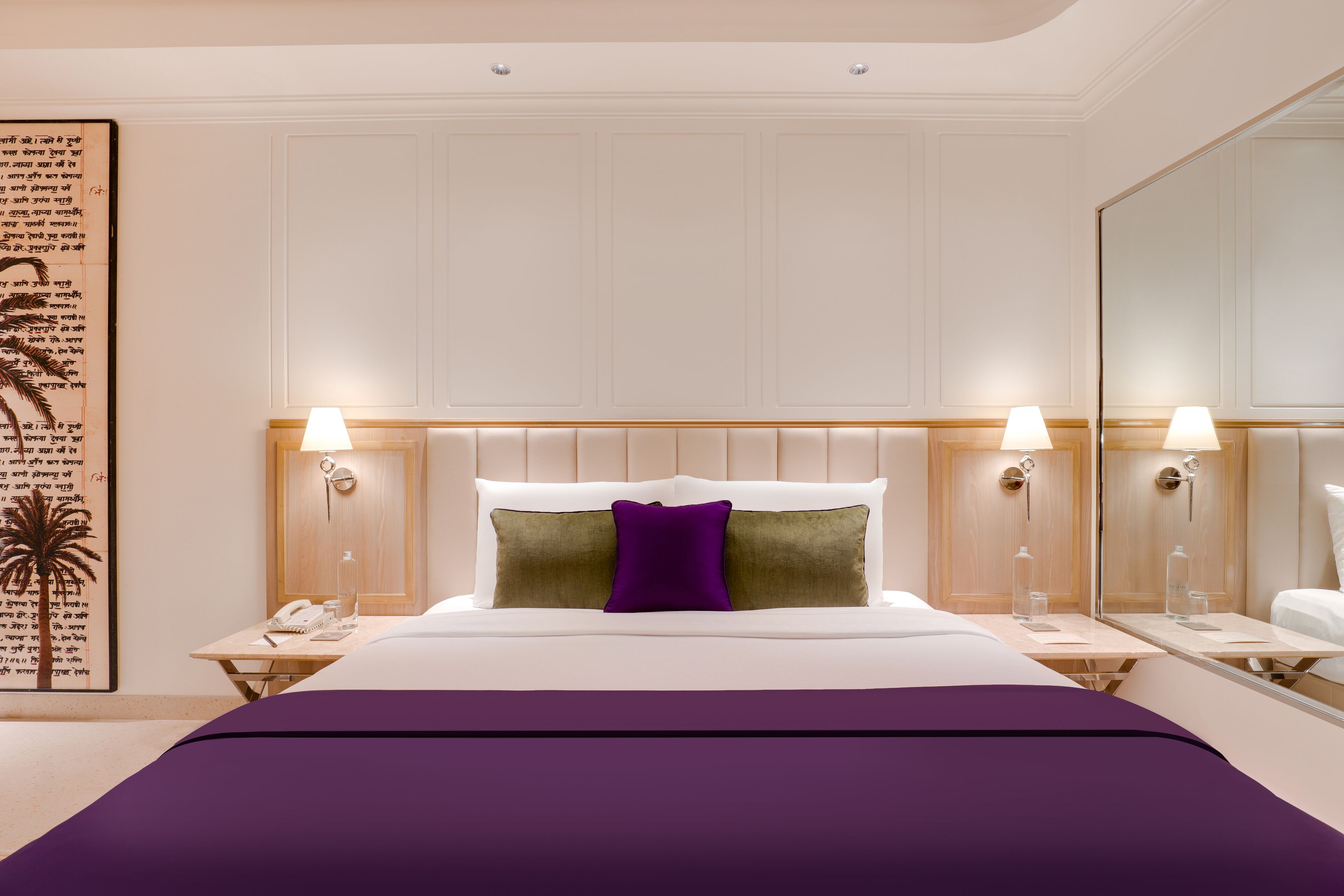 A hotel room with a large bed, two bedside tables, a nightstand, a mirror, and a wall with a decorative piece.