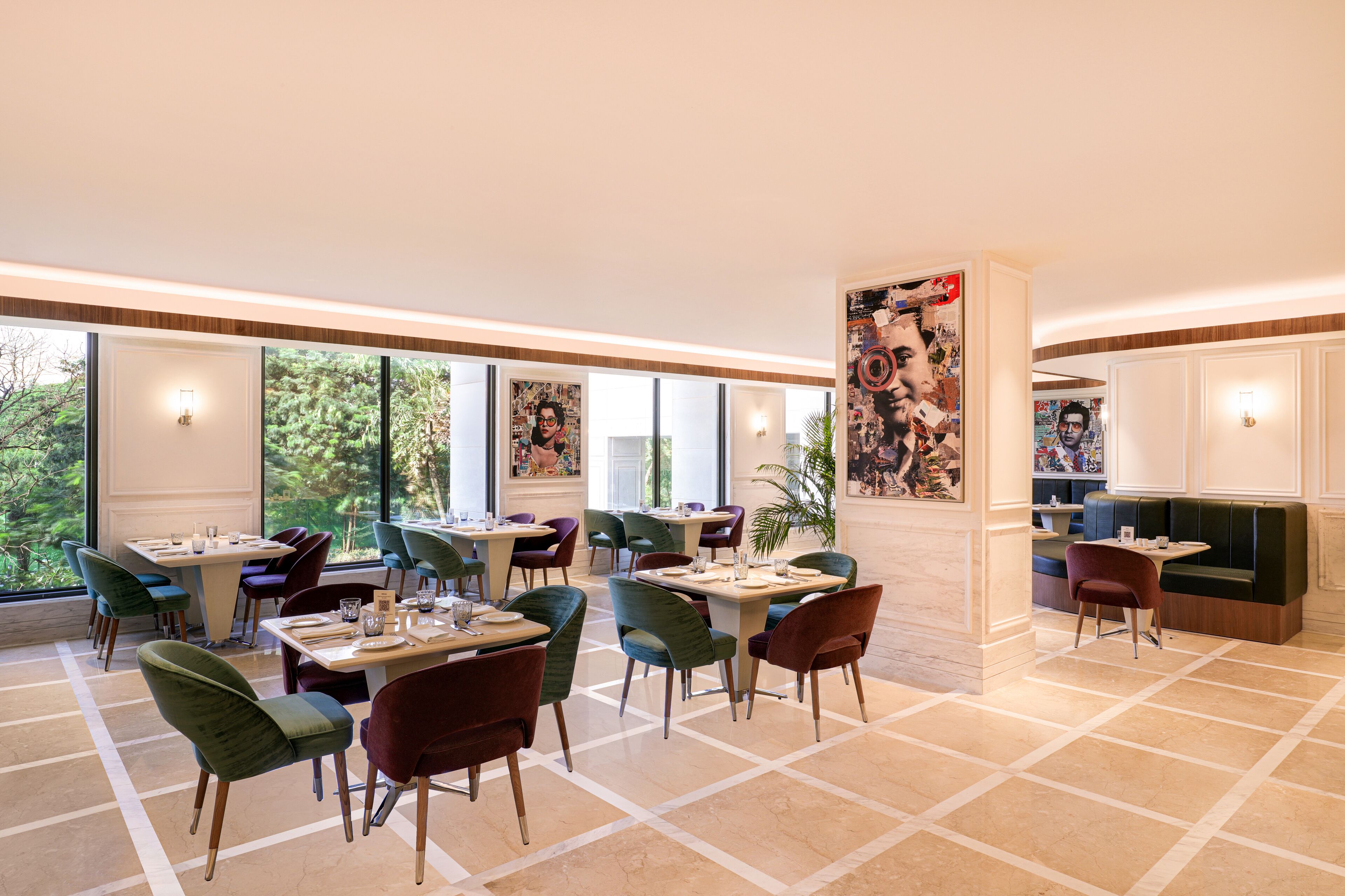 A modern dining area with multiple tables and chairs, large windows offering a view of the outdoors, and a central column with artwork.
