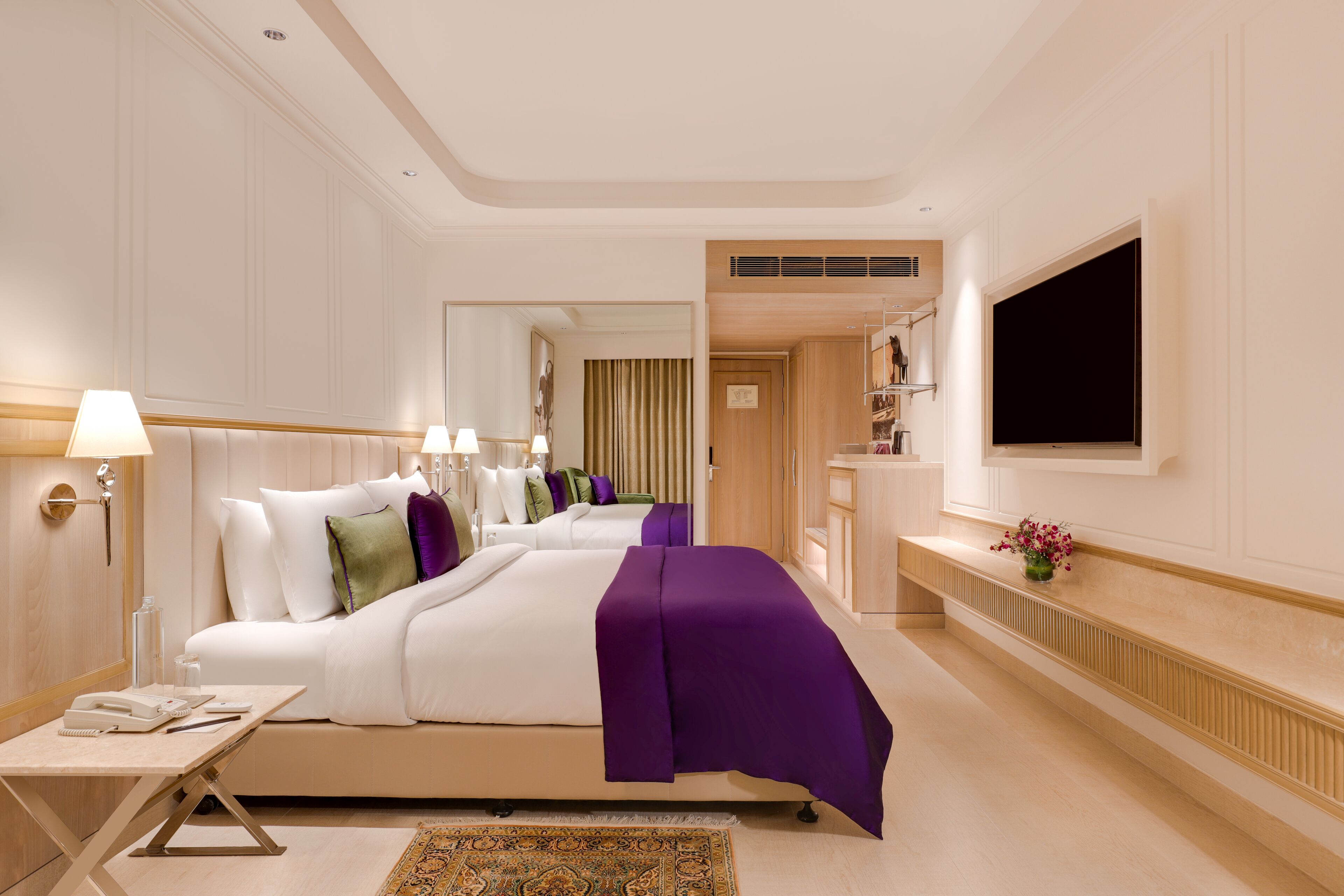 Una habitación de hotel con una cama grande, un escritorio con lámpara, un televisor montado en la pared y una pequeña mesa con un jarrón de flores.