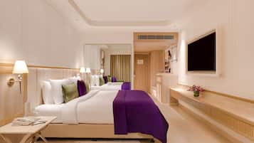 Una habitación de hotel con una cama grande, un escritorio con lámpara, un televisor montado en la pared y una pequeña mesa con un jarrón de flores.