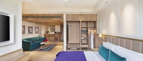 A modern hotel room with a large bed, a seating area with a sofa, a TV, and a kitchenette.