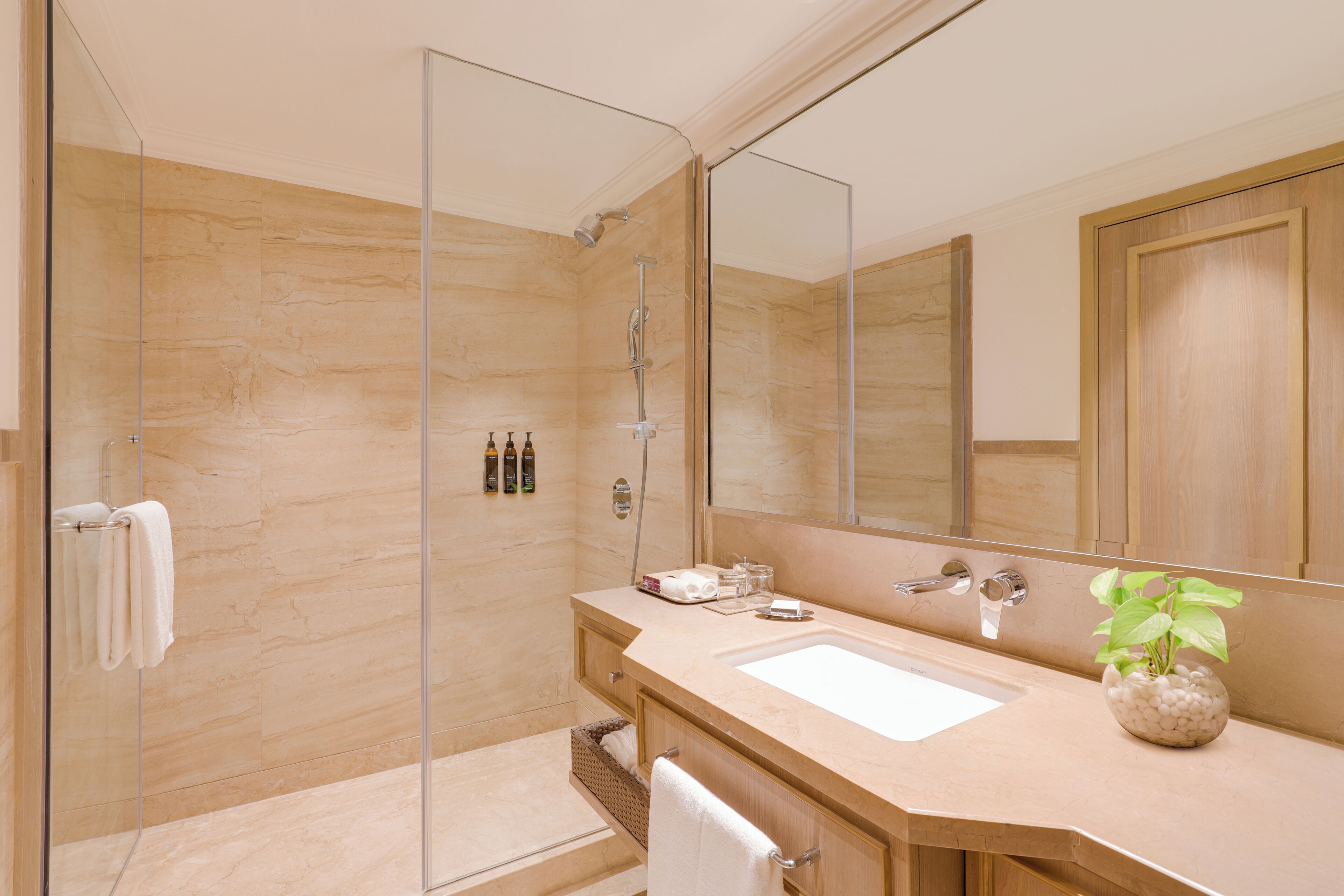 Un baño moderno con ducha de vidrio, un espejo grande y un lavamanos con un florero.