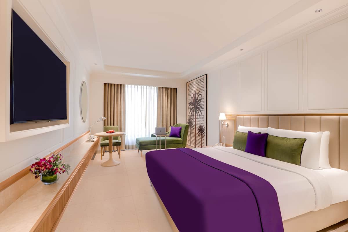 Une chambre d’hôtel avec un lit, un bureau, une chaise, une télévision et une fenêtre avec des rideaux.