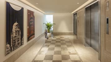 A hallway with checkered flooring, a potted plant, and a large painting of a building.
