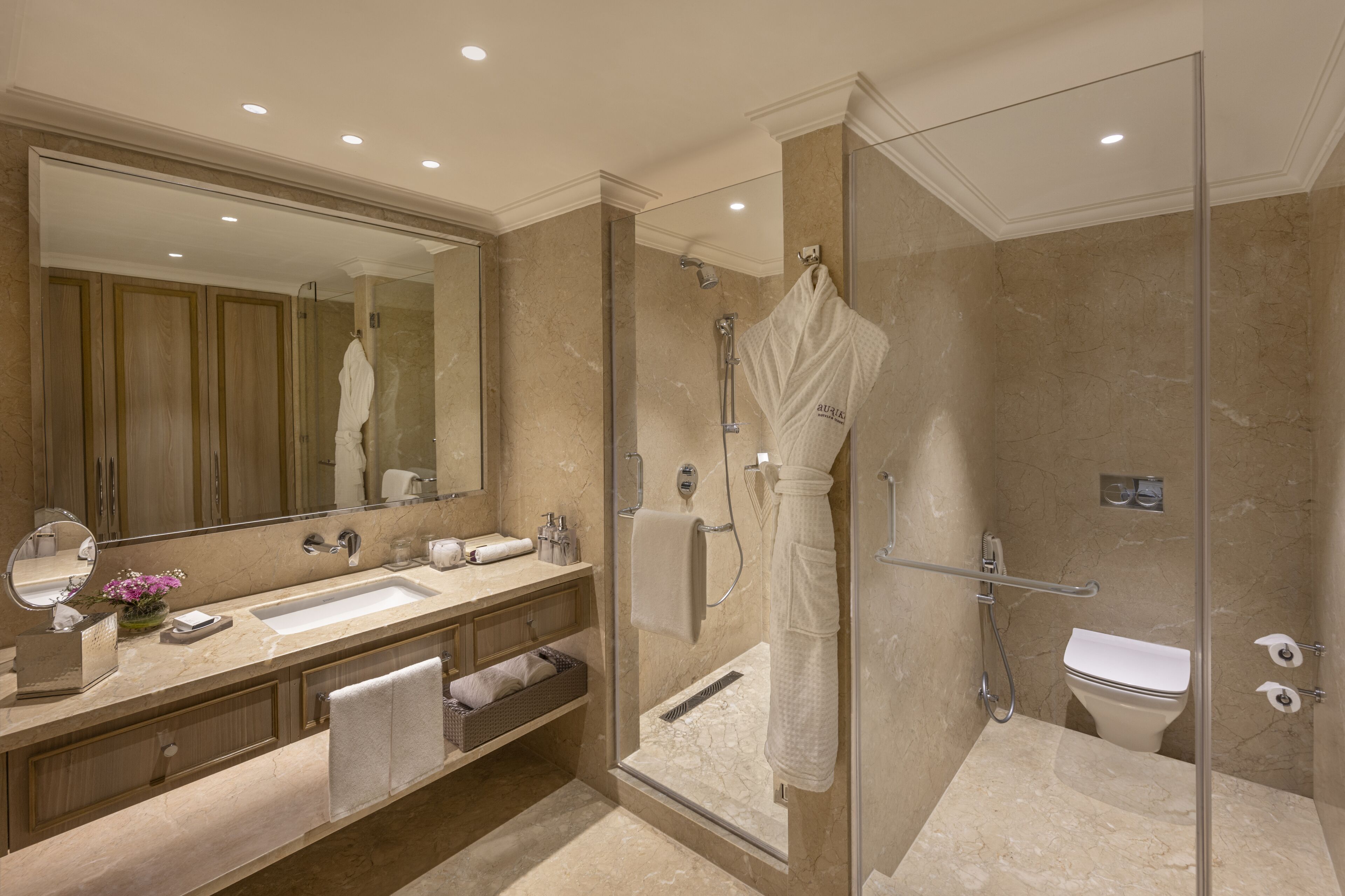 Un baño moderno con ducha envuelta en vidrio, un espejo grande y tocador con lavamanos y toallero.