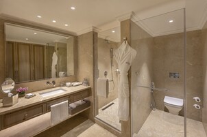 Un baño moderno con ducha envuelta en vidrio, un espejo grande y tocador con lavamanos y toallero.