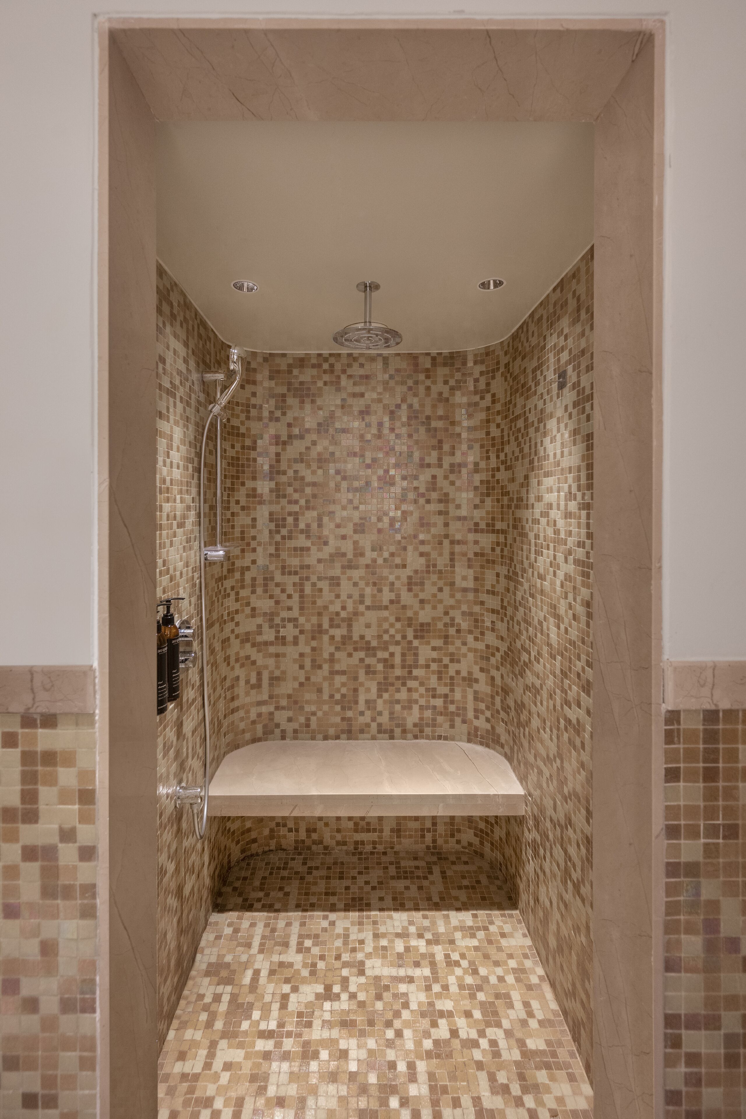 Een douche met betegelde muren en vloer, een inbouwbank en een handdouche.