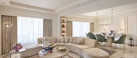 A spacious living room with a curved sectional sofa, a round coffee table, and a dining area with a chandelier.