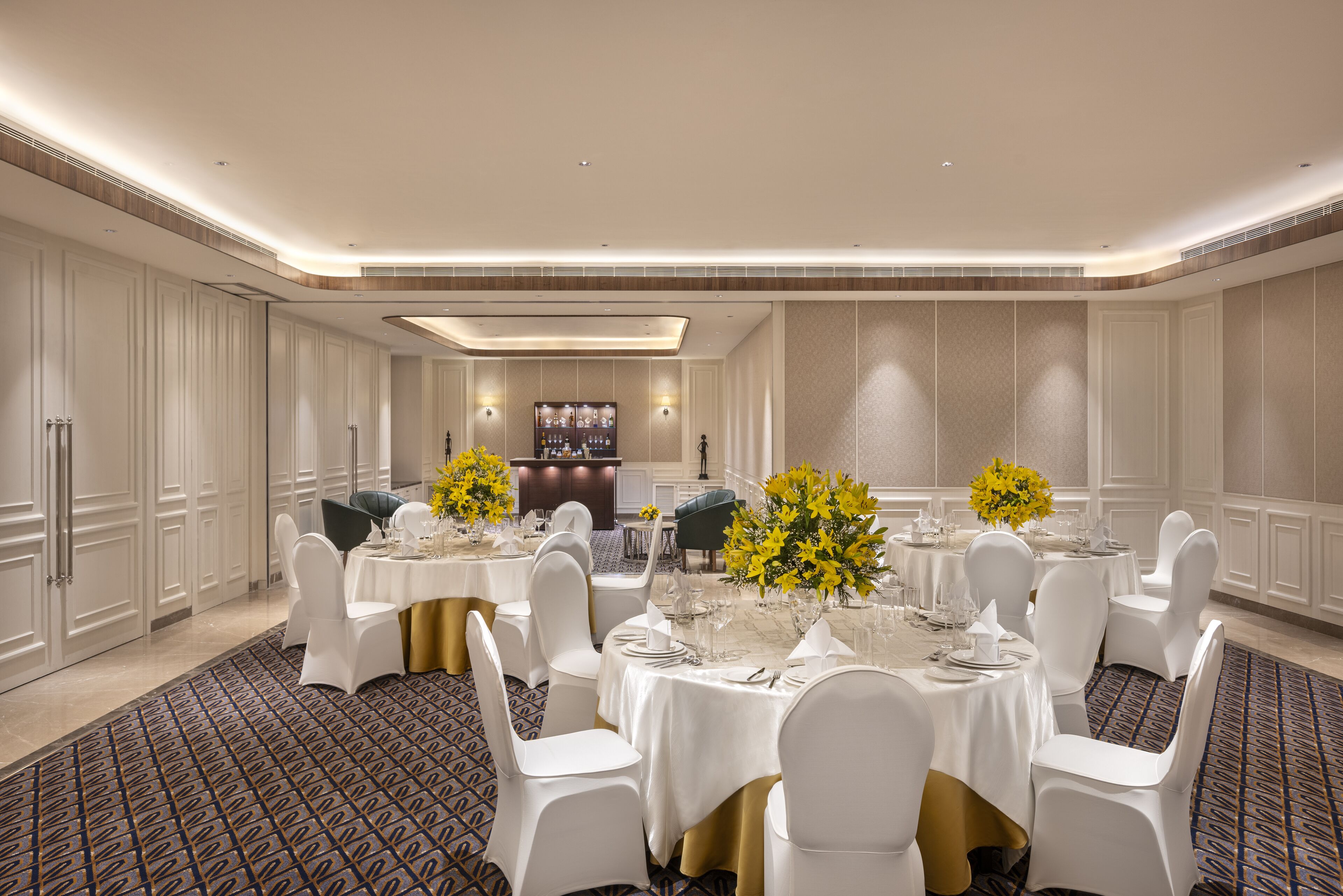 A formal dining room with round tables, white chairs, and yellow flowers.