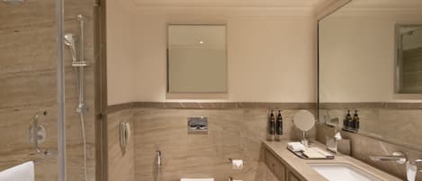 Un baño moderno con ducha envuelta en vidrio, inodoro blanco, espejo grande y tocador con artículos de aseo.