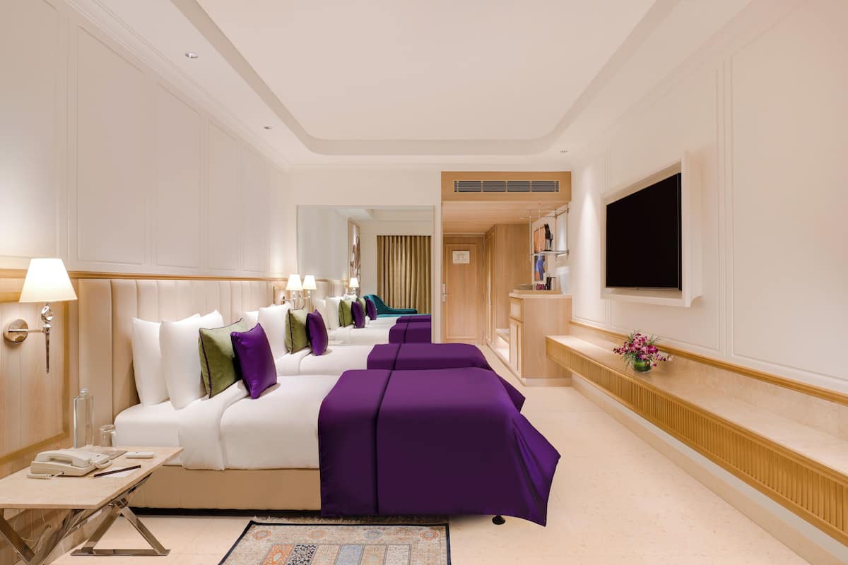 Une chambre d’hôtel avec un grand lit, un bureau avec une lampe, un téléviseur fixé au mur et une petite table sur laquelle est posé un vase de fleurs.