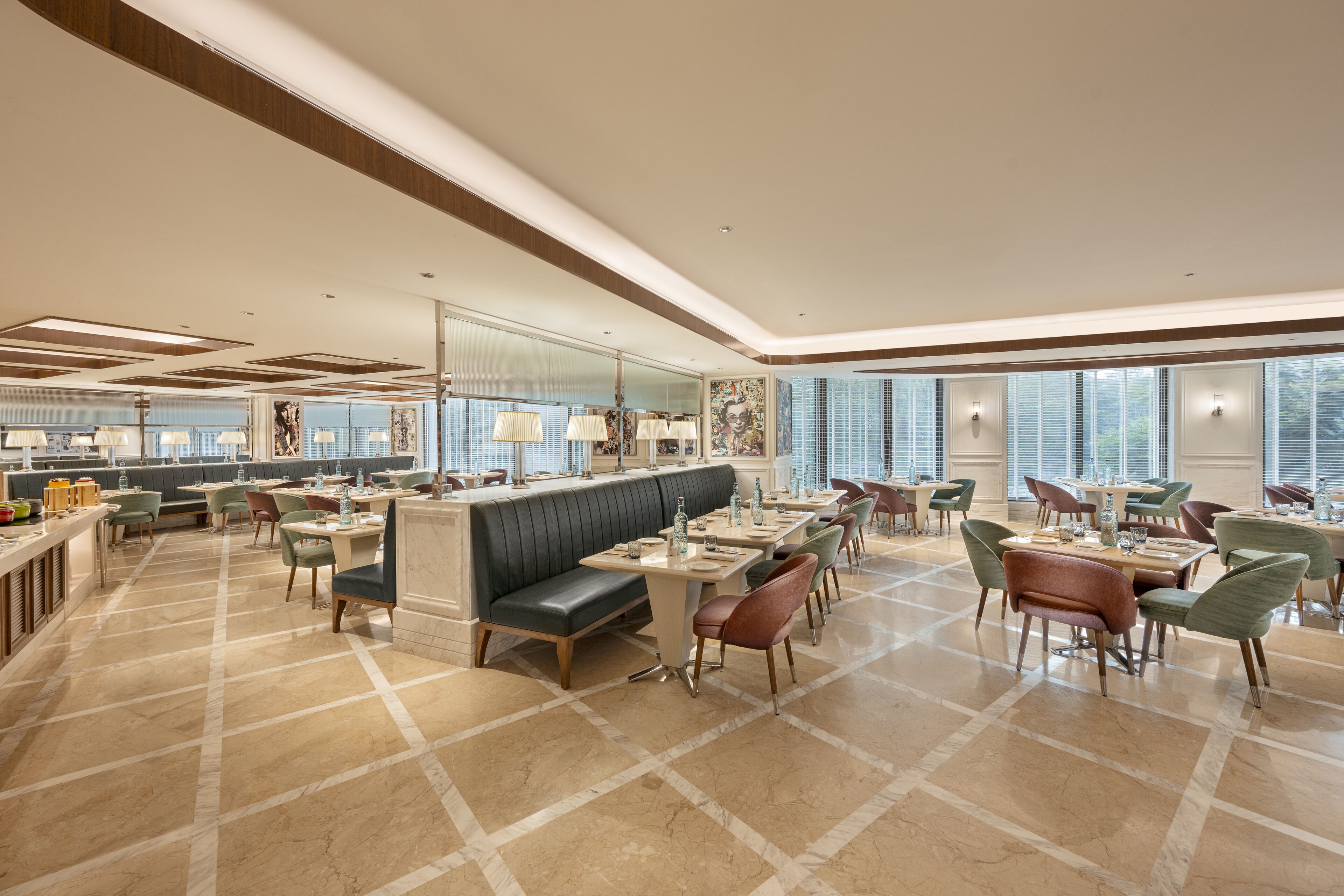 Un hall d’hôtel spacieux doté d’un espace salon central, de plusieurs tables à manger et de grandes fenêtres laissant entrer la lumière naturelle.