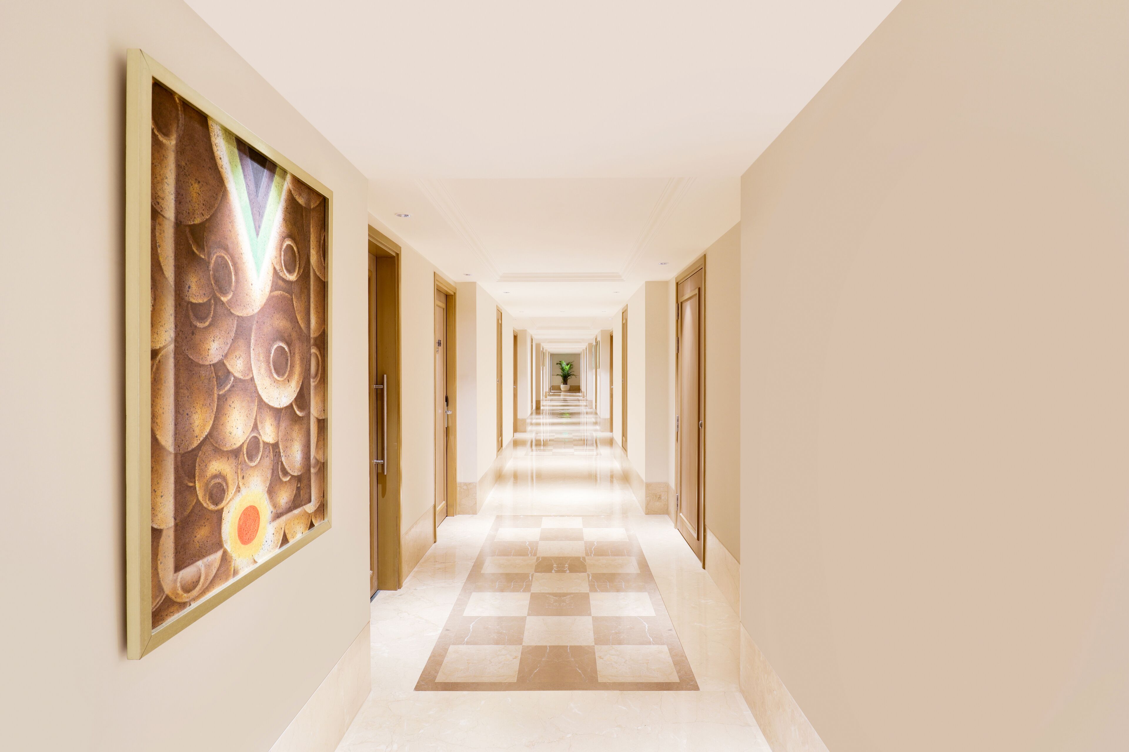 A hotel corridor with a checkered floor, doors on both sides, and a framed artwork on the left wall.