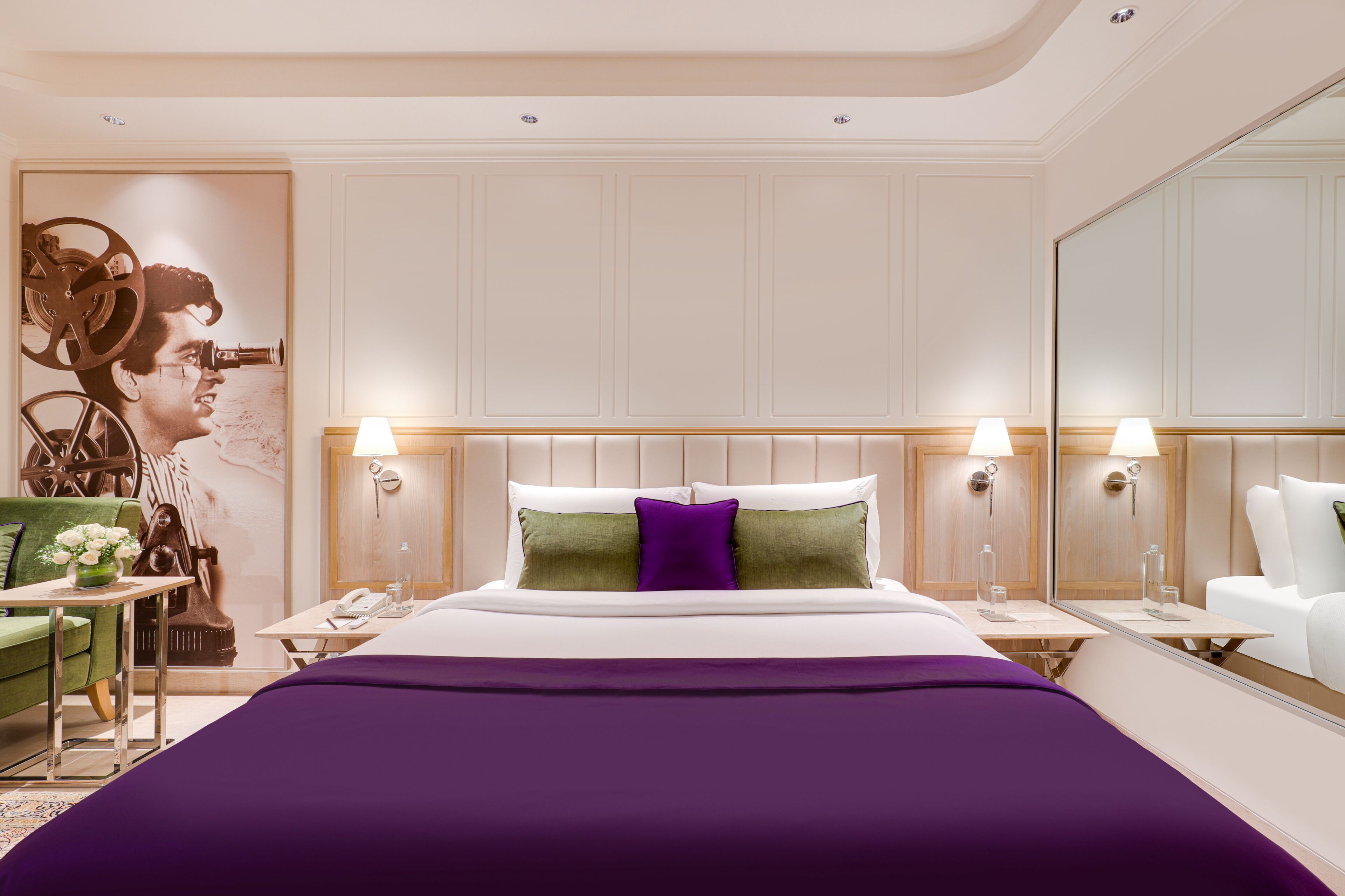 Una habitación de hotel con una cama grande, dos mesitas de noche, un tocador, un espejo y una pared con un cartel decorativo.