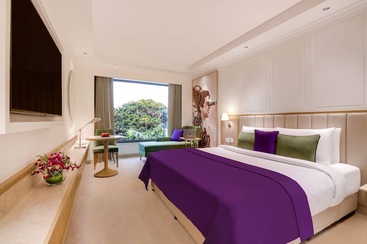 Une chambre d’hôtel moderne, dotée d’un grand lit, d’un bureau et offrant une vue sur la verdure environnante.