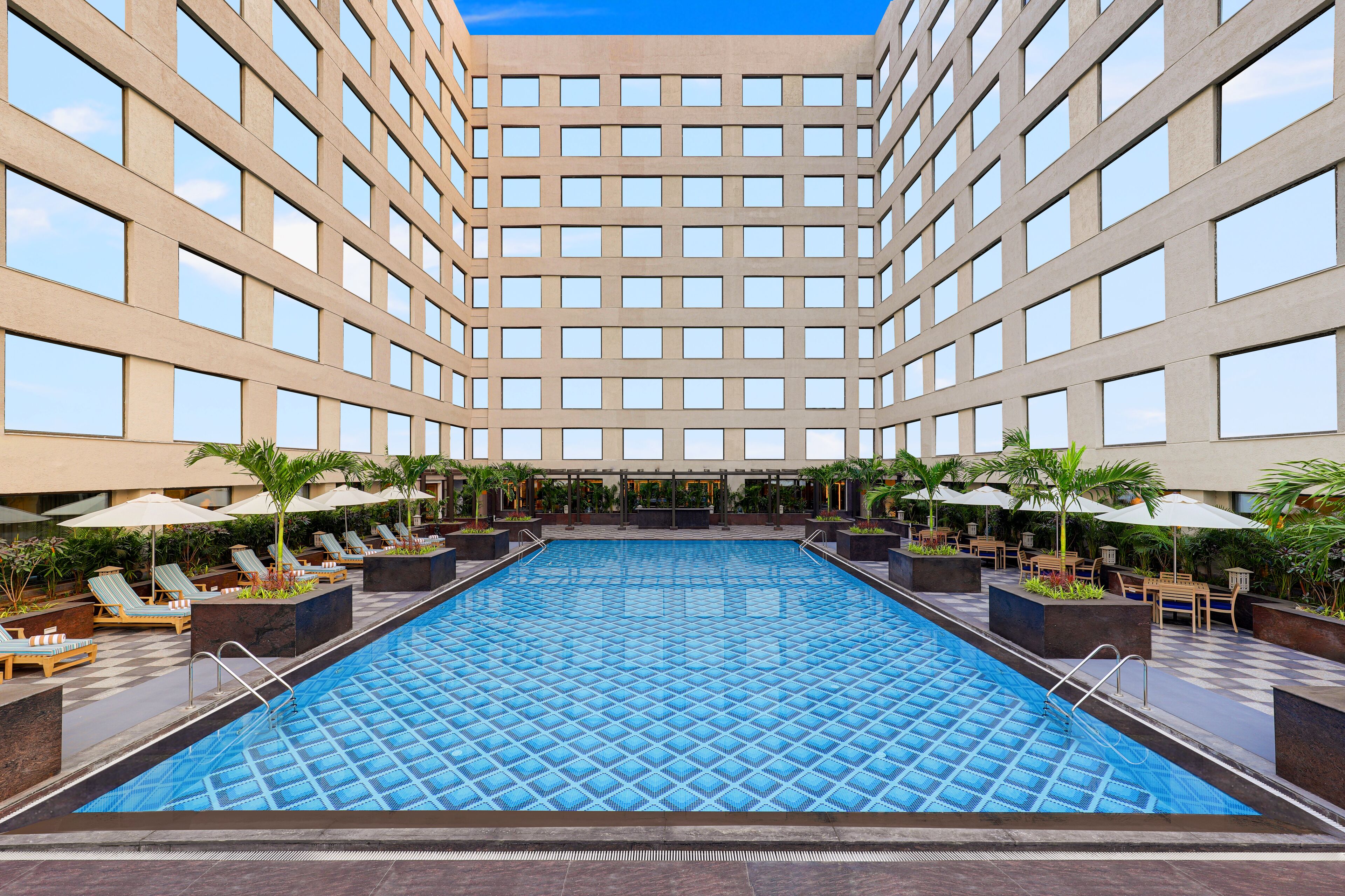 A large indoor swimming pool with lounge chairs and umbrellas, surrounded by a high-rise building with many windows.