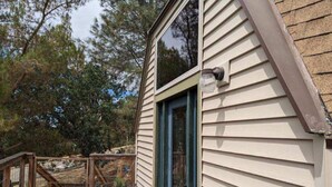 A wooden deck with a glass door leading to a building with beige siding and a blue window frame.