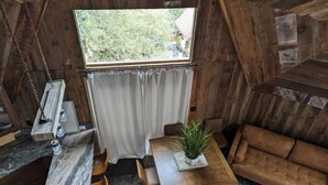 A cozy room with a wooden ceiling, a small table with a plant, a sofa, and a window with curtains.
