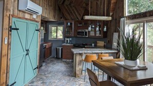 A rustic kitchen with wooden walls, a stone floor, a teal door, and a large window.