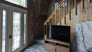 A wooden interior with a TV on a wooden stand, a staircase, and a door with stained glass.