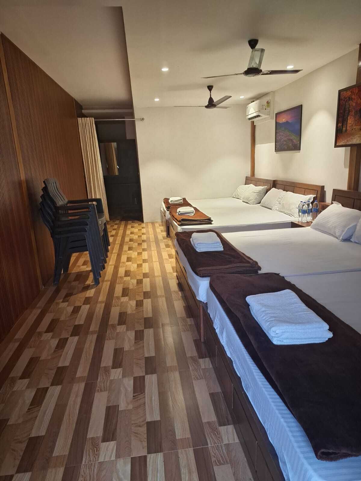 A hotel room with two beds, a wooden floor, a ceiling fan, and a painting on the wall.