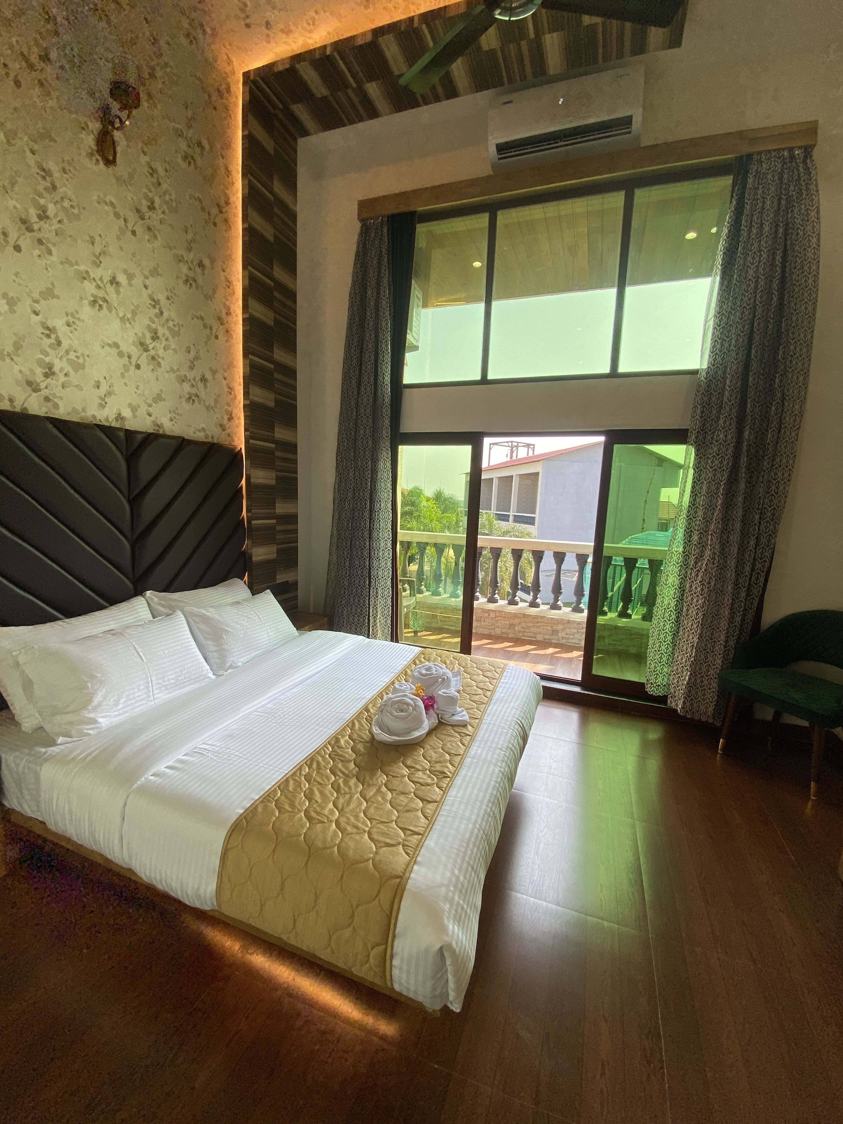 A hotel room with a large bed, a headboard, a window with curtains, and a view of the outside balcony.