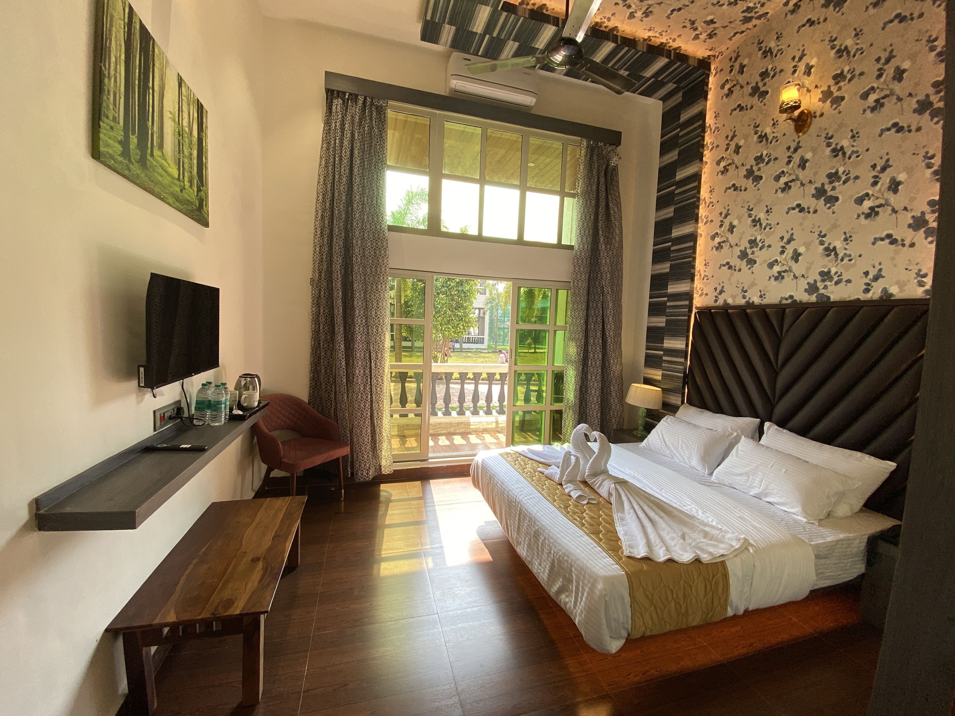 A hotel room with a bed, a desk, a chair, a TV, and a large window with curtains.