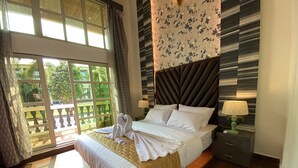 Habitación de hotel con una cama grande, vistas a través de un ventanal, un cabecero estampado y una mesita de noche con una lámpara.