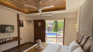 Habitación de hotel con cama, televisión, techo de madera y vista a una piscina.