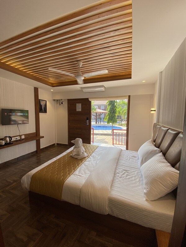 A hotel room with a bed, a TV, a wooden ceiling, and a view of a pool. - DAN Resorts & Weddings (Dahanu)