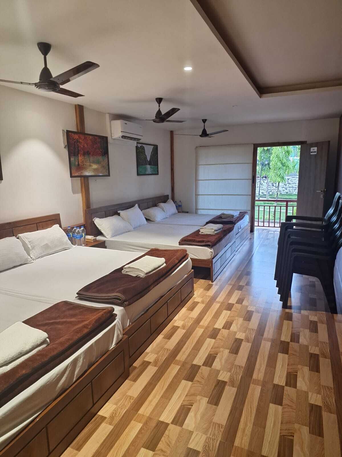 Habitación de hotel con dos camas, ventiladores de techo, suelo de madera y vistas a zonas verdes.