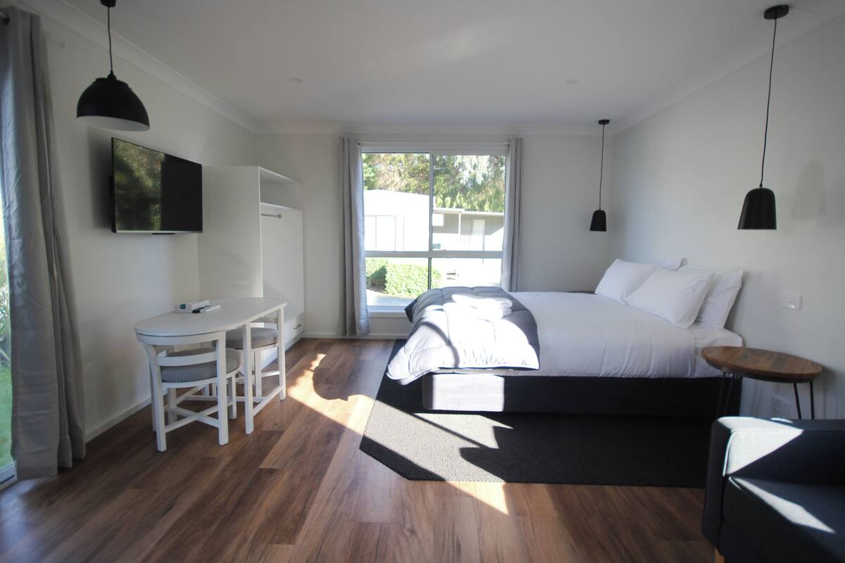 Un dormitorio con cama, mesita de noche y escritorio con silla.