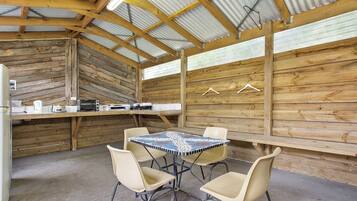 A rustic wooden interior with a tiled table and four chairs, a wooden counter with kitchen appliances, and a corrugated metal roof.