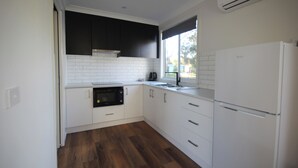 A kitchen with white cabinets, a black oven, and a white refrigerator. - Wonthaggi Park Lane Holiday Park (Wonthaggi)