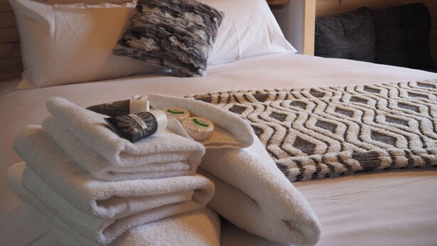 A neatly made bed with a patterned blanket, a stack of folded towels, and a few toiletries on the bed. - Wonthaggi Park Lane Holiday Park (Wonthaggi)