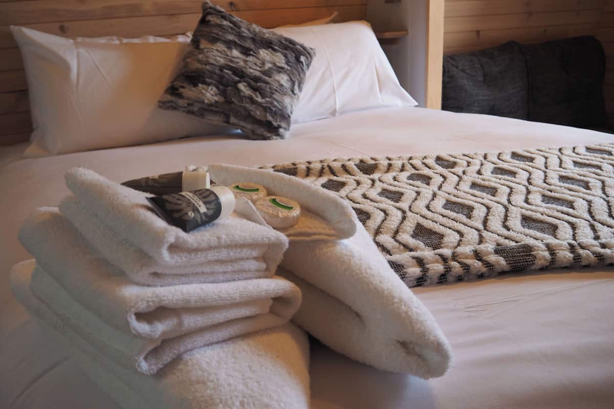 Una cama bien hecha con un edredón estampado, una pila de toallas dobladas y algunos artículos de tocador sobre la cama.