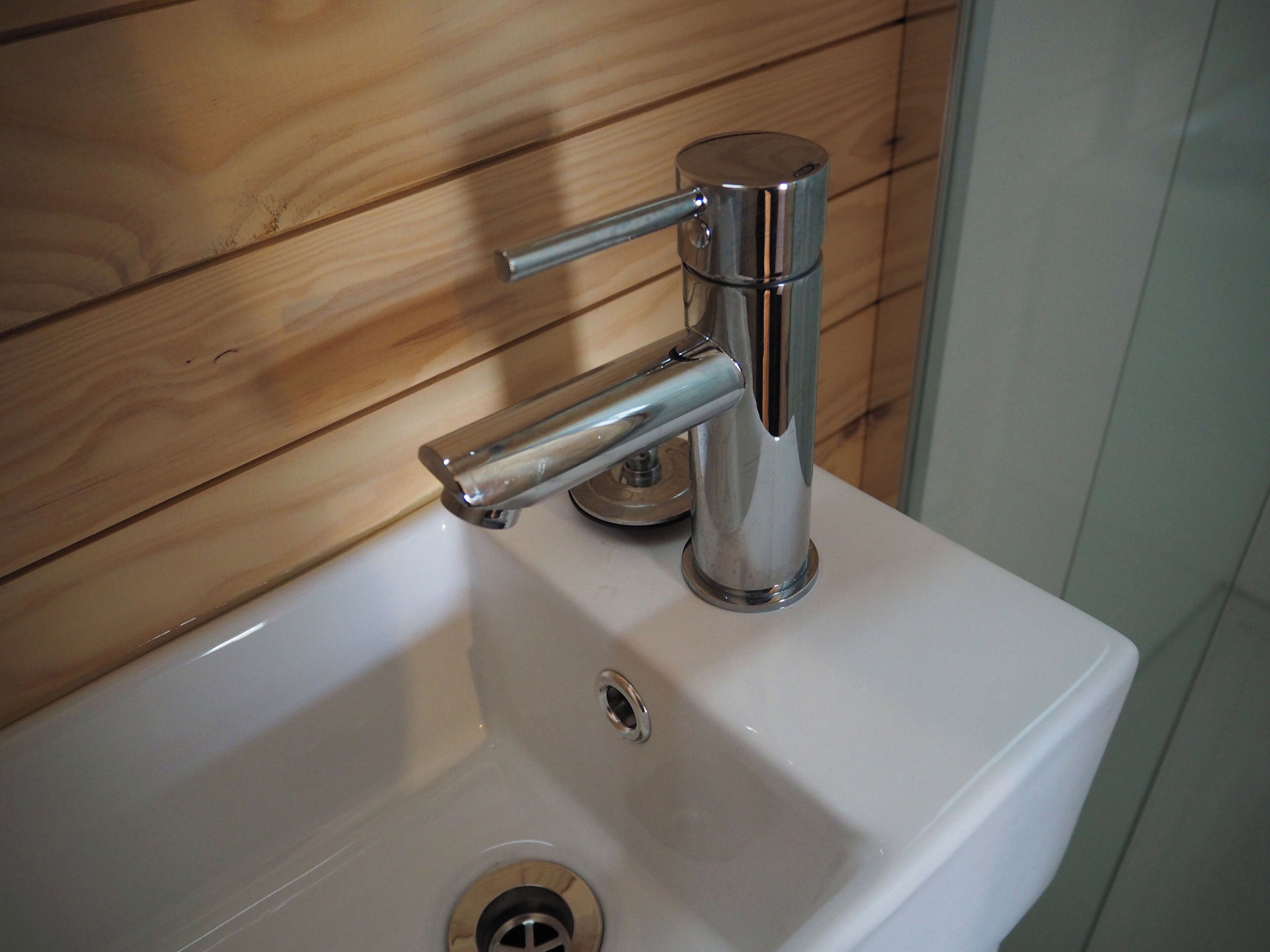 A bathroom sink with a chrome faucet and a wooden panel background.